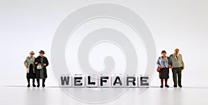 Two miniature old couple standing and white cubes with `WELFARE` letters.