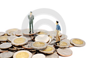 Two miniature people walking and standing on pile of new Thai Baht coins, isolated on white background.