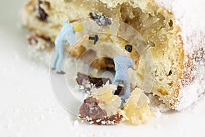 Two miniature worker breaking little pieces out of a christmas stollen filled with raisins
