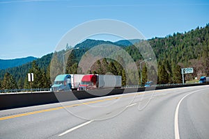 Two modern colored semi trucks driving highway turn side by side