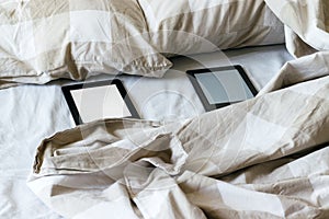 Two modern electronic books with a blank empty screens on a white and beige bed. Mockup family tablets on bedding