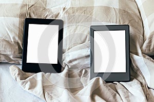 Two modern electronic books with a blank empty screens on a white and beige bed. Mockup tablets on bedding