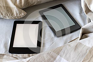 Two modern electronic books with a blank screens on a white and beige bed. Mockup tablets on bedding