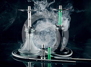 Two modern hookahs with smoke on a black mirror background