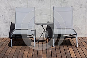 Two Modern Lounge Chairs and a Side Table on a Wooden Deck Under Sunlight