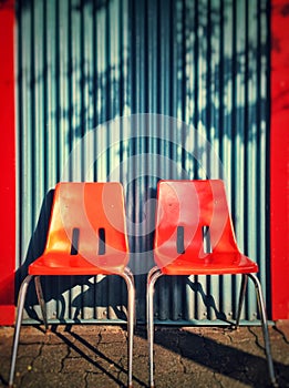 Two modern orange plastic chairs against a blue corrugate wall. photo