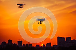Two modern Remote Control Air Drones Fly with action cameras in dramatic orange sunset sk