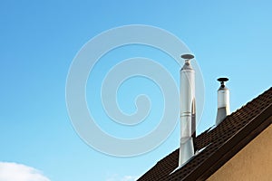 Two modern style chimneys from oven and fireplace stacked stainless steel on tiled roof made according to fire safety requirements