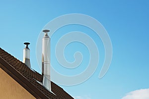 Two modern style chimneys from oven and fireplace stacked stainless steel on tiled roof made according to fire safety requirements