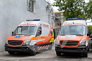 Two modern white and orange ambulance medical emergency vans truck parked near hospital building. Paramedic vehicles on