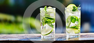 Two mojito cocktails with lime and ice on wooden table top