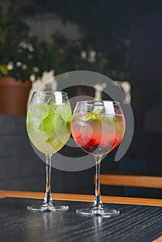 Two mojito on the table. Two alcohol cocktails in tall glasses with berries and mint on a wooden table