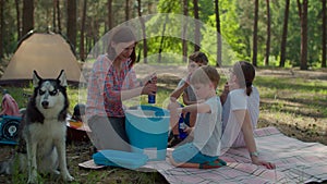 Two moms and two sons drinking cold beverages from fridge on picnic blanket during summer family camping vacation with