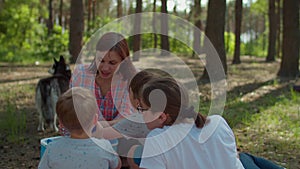 Two moms and two sons drinking cold beverages from fridge on picnic blanket during summer family camping vacation with