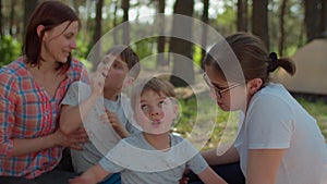 Two moms, two sons and Siberian Husky dog resting on picnic blanket during summer family camping vacation with tent in