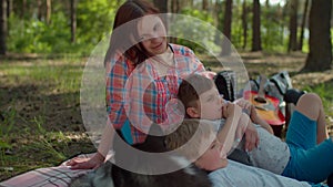 Two moms, two sons and Siberian Husky dog resting on picnic blanket during summer family camping vacation with tent in