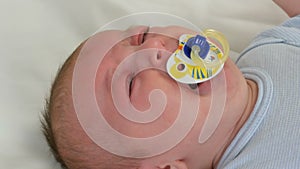 Two month old newborn baby cries loudly with pacifier in mouth. Child face close up view
