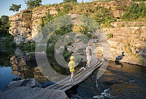 Two - mother and son, walk along the bridge across the mountain river against the backdrop of natural landscape