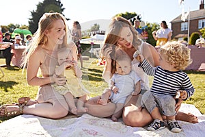 Two Mothers With Children On Rug At Summer Garden Fete