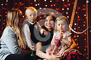 Two mothers sitting with cute kids christmas presents.