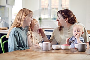 Two Mothers With Young Children Sitting Around Table On Play Date With Fruit Snacks