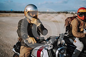 two motorcycle riders with helmets talking on their motorcycles and one man is wearing his hands