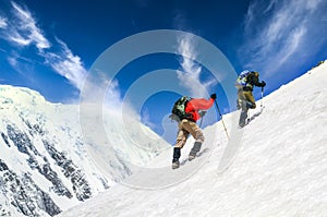 Two mountain trekkers on steep snowed hill with dramatic sky background