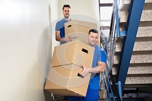 Two Movers Carrying Cardboard Boxes On Staircase