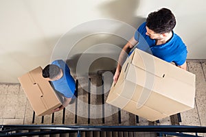 Two Movers Carrying Cardboard Boxes On Staircase