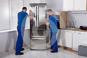 Two Movers Placing Refrigerator In Kitchen