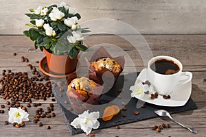 Two muffins, cup of aroma coffee, coffee grains and flowers of azalia on gray wooden background.