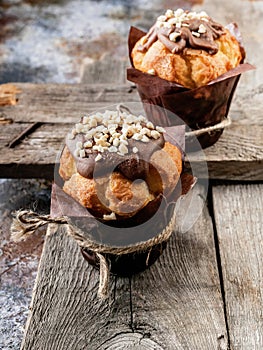 Two muffins with milk chocolate and nuts on a rustic wooden background. Close-up
