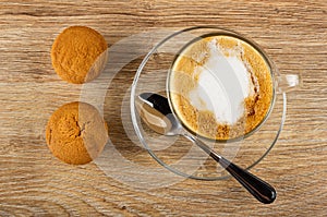 Two muffins, spoon, cappuccino in glass cup in saucer on wooden table. Top view