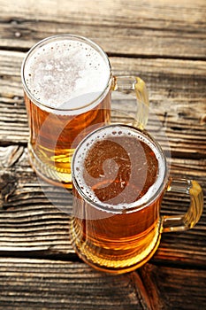 Two mug of beer on brown wooden background.