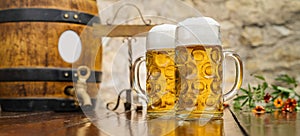 Two mugs of beer with foam and wooden barrel stand on the table, Oktoberfest, Munich, Germany