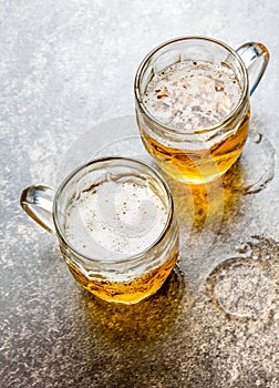 Two mugs of beer on stone background. Close up.