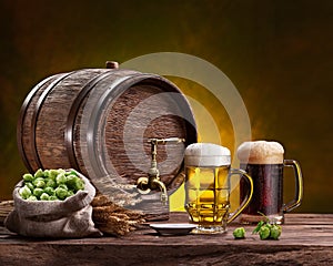 Two mugs of chilled beer, beer cask and bag of beer hops on wooden table