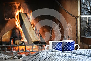 Two mugs (cup) of tea or coffee in front cozy and worm fireplace, in country house.