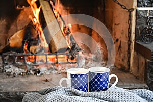 Two mugs (cup) of tea or coffee in front cozy and worm fireplace, in country house.