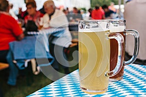 Two mugs with a light and dark beer stand on the table. In the background, blurred people. Celebrating the traditional