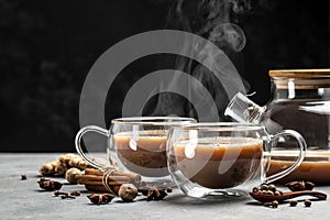 Two mugs of masala tea. Hot indian masala chai tea with milk and spices in a glass glass on dark background. place for text