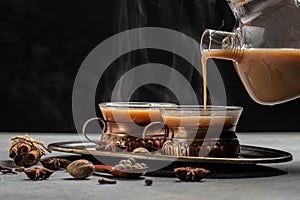 Two mugs of masala tea. Hot indian masala chai tea with milk and spices in a glass glass on dark background. place for text