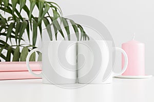 Two mugs mockup with books and a candle on a white table and a palm plant