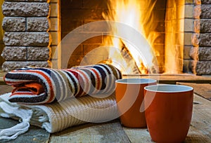 Two mugs for tea or coffee, woolen things near cozy fireplace.