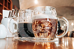 Two mugs of white and dark beer in pub.