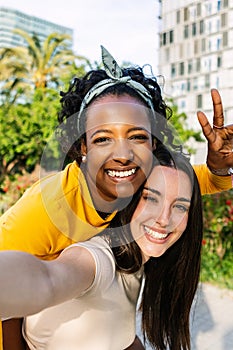 Two multi ethnic female friends taking self portrait with mobile phone outdoors