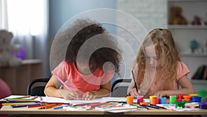 Two multi-racial girls drawing with colorful pencils in early education center photo
