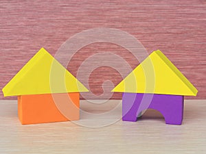 Two multicolored yellow, purple, orange house of building blocks triangle, rectangle, a children educational toy on a pink bac