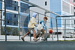 Two multicultural boys in activewear playing basketball outdoors