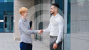 Two multiethnic colleagues arab man and caucasian woman business partners handshaking outdoors near company building